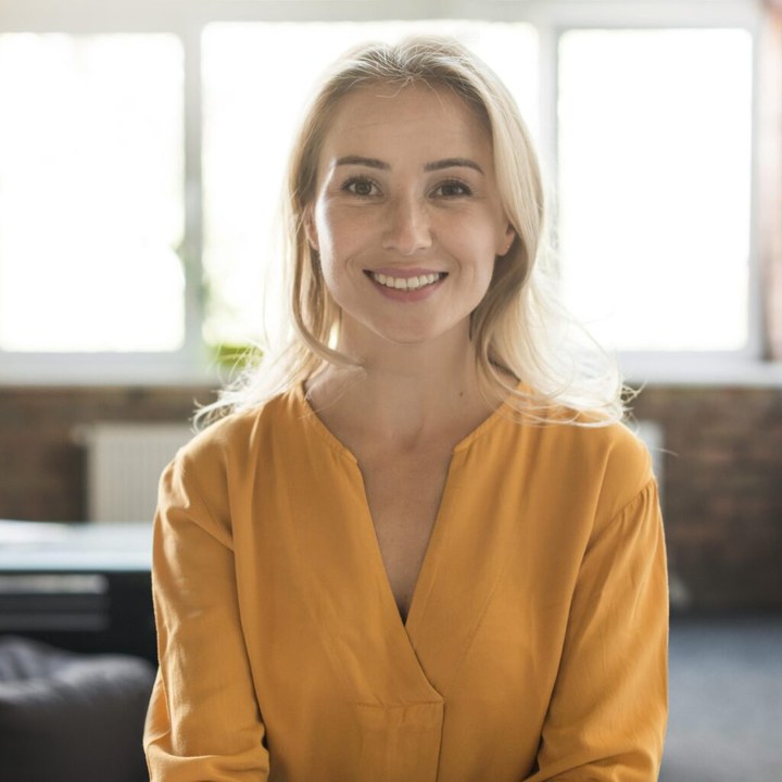 A smiling woman in a mustard blouse standing in a bright room